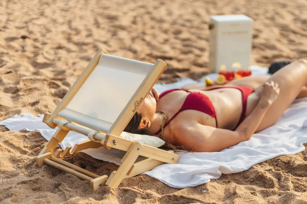 Woman in red bikini lying on a towel with a SunDoze Headrest and  sandy beach.