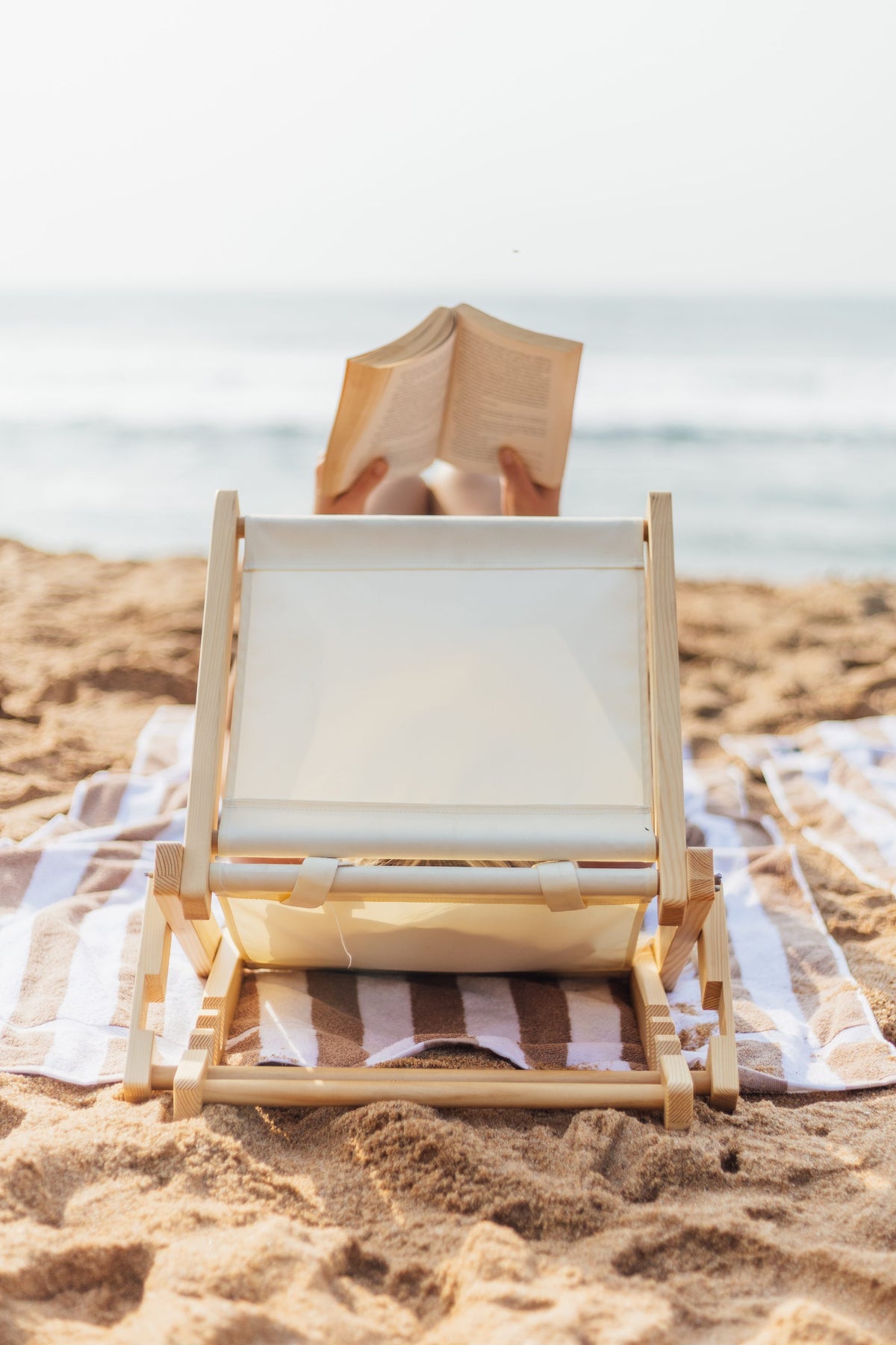 Person reading a book behind a SunDoze beach headrest, facing the sea
