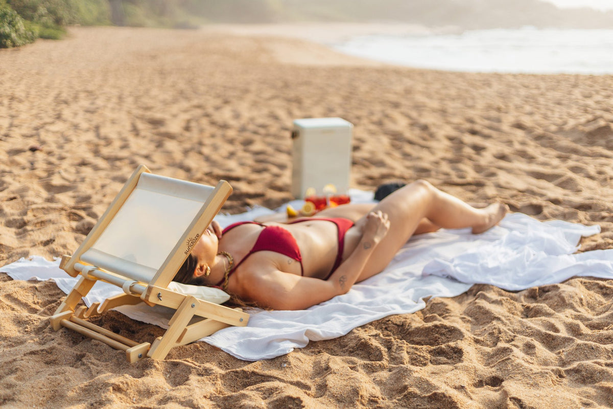 Woman napping on a beach towel with a SunDoze headrest shading her face
