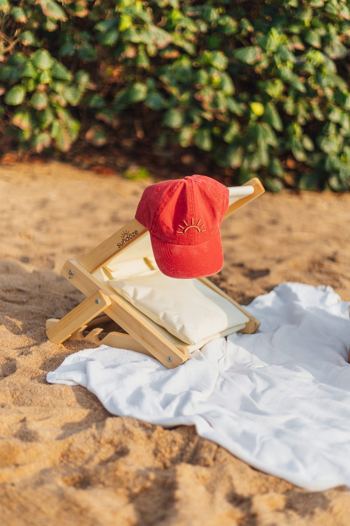 Red SunDoze cap resting on a SunDoze headrest on a white beach towel