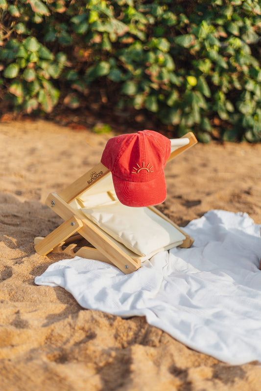 Red SunDoze cap resting on a SunDoze headrest on a white beach towel